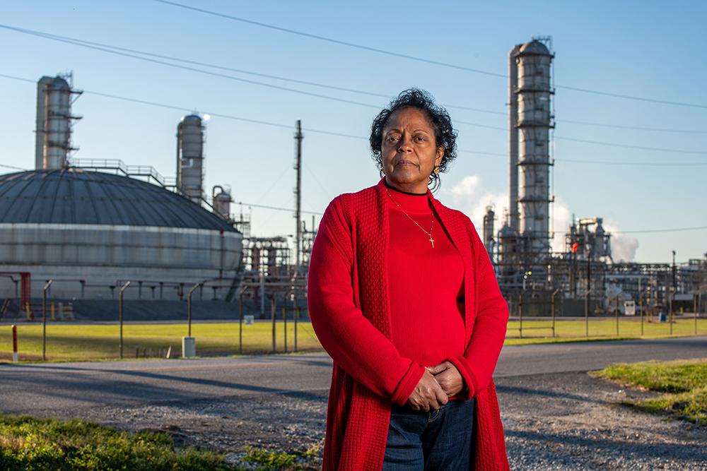 Woman in a red cardigan standing in front of a petrochemical refinery